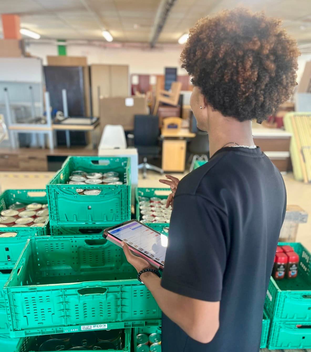 Une personne utilise la tablette au milieu des caisses de denrées, dans l’atelier Stëmm iessen.